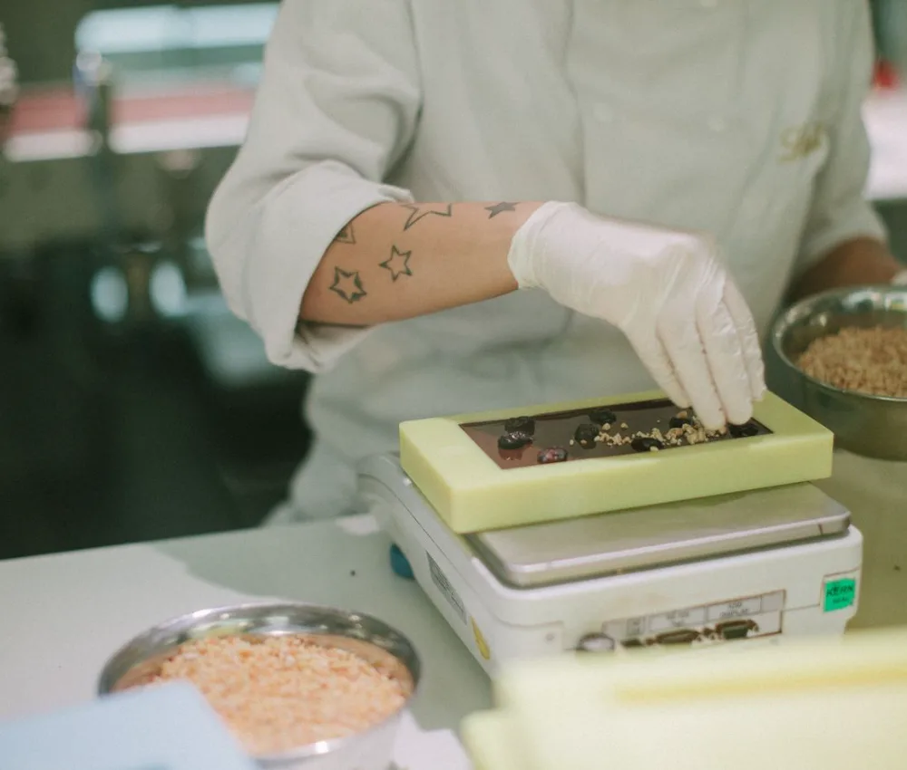 Gloved worker weighing a chocolate bar on a scale during a quality check